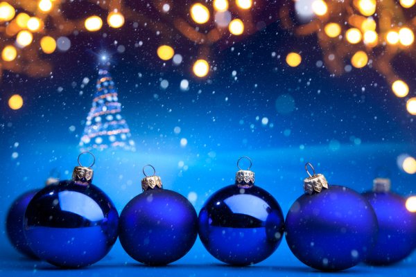 Vijf blauwe kerstballen met vallende sneeuw op de voorgrond, op de achtergrond vage gele lichtjes en een kerstboom.