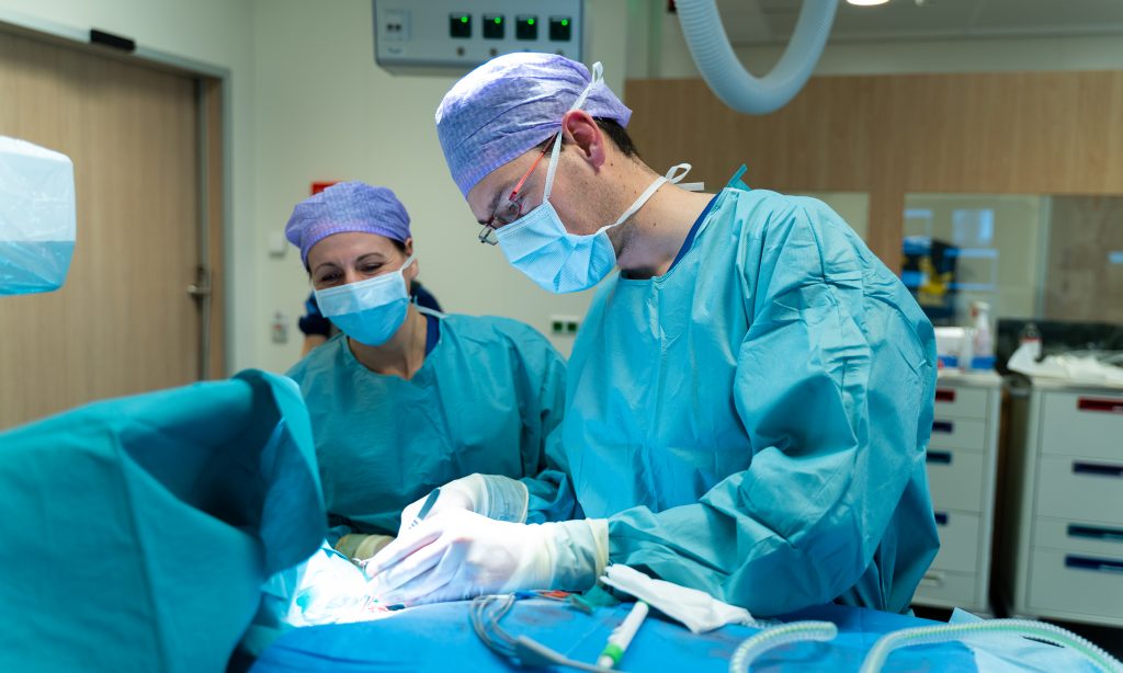 Twee chirurgen in blauwe kleding voeren een operatie uit in het Catharina Ziekenhuis. Medische apparatuur op de achtergrond.