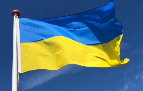 Oekraïense vlag met blauw en geel wappert aan een witte vlaggenmast tegen een heldere blauwe lucht.