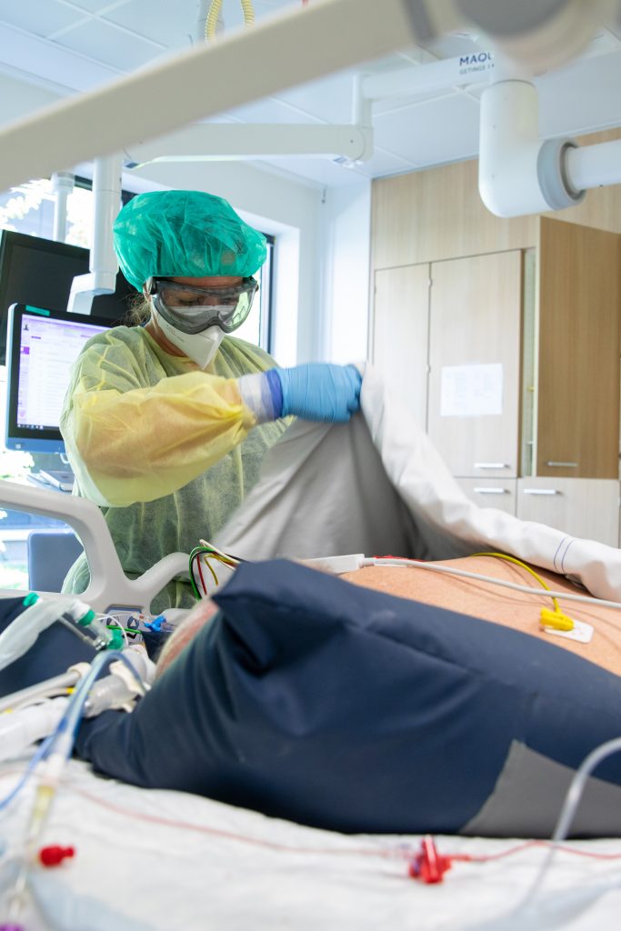 Zorgmedewerker in beschermende kleding past deken aan bij patiënt in Santeon-bed met medische apparatuur en slimme software.