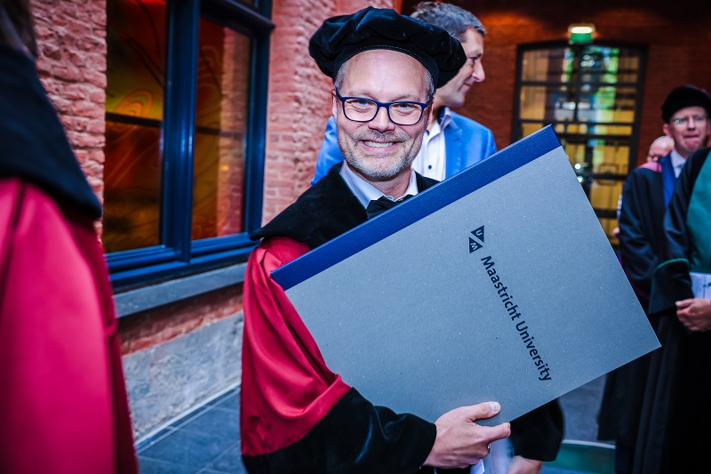 Koen Rovers, kunstonderzoeker, in toga met diploma van Universiteit Maastricht, viert promotie cum laude op afstudeerevenement.