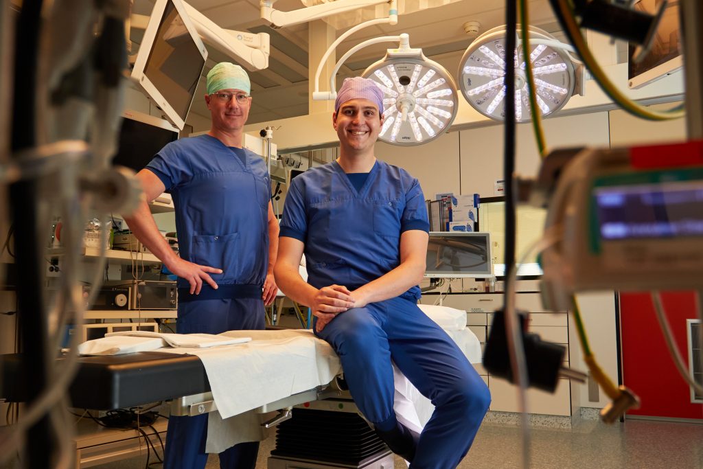 Twee chirurgen in blauwe werkkleding staan in de OK van het Catharina Hart- en Vaatcentrum, omringd door medische apparatuur.