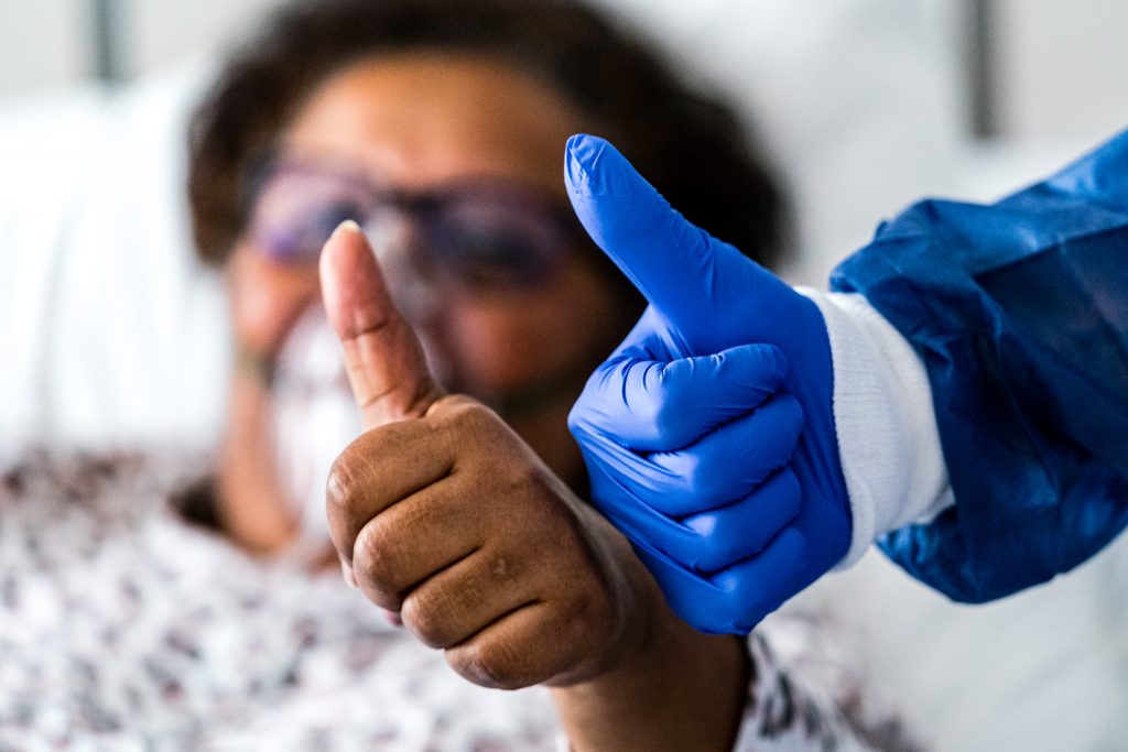 Patiënt in bed bij Catharina Ziekenhuis en zorgmedewerker geven beide duim omhoog; handen scherp, patiënt wazig.