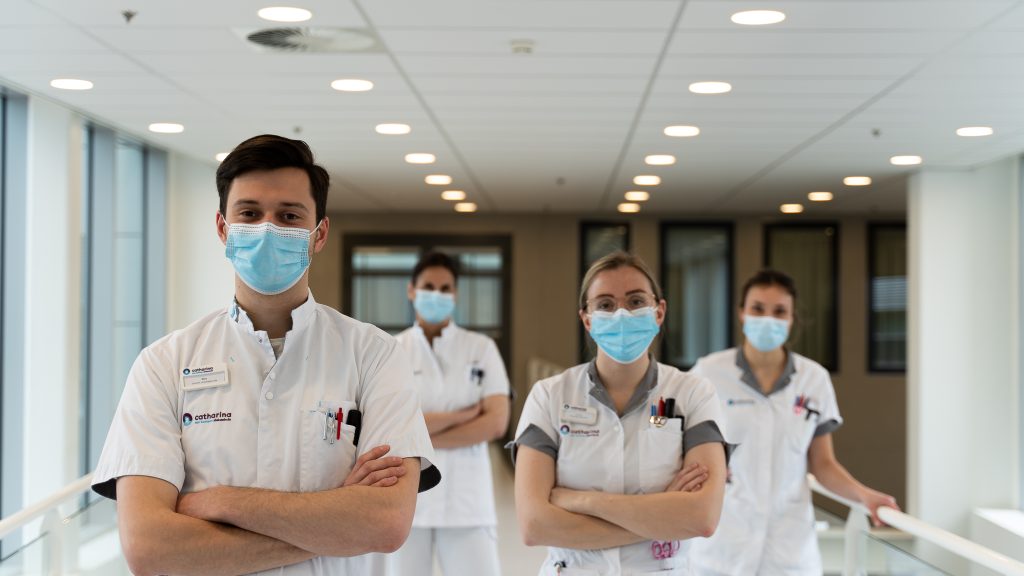 Vier zorgprofessionals in witte uniformen en mondmaskers staan met gekruiste armen in een gang van het Catharina Ziekenhuis.