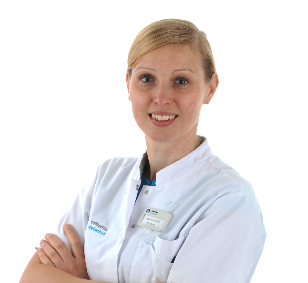 Vrouw met blond haar in witte doktersjas en badge, gekruiste armen, glimlacht voor huidscan op effen witte achtergrond.