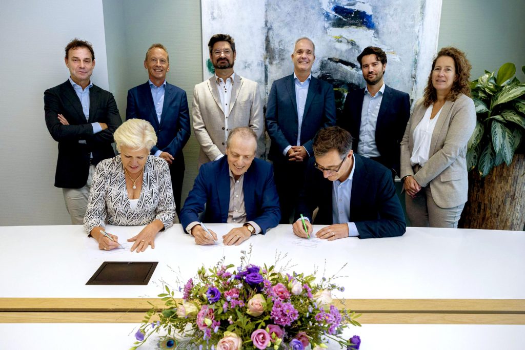 Negen personen in vergaderruimte; drie ondertekende documenten over digitale zorg, zes staan erachter. Bloemen op tafel.
