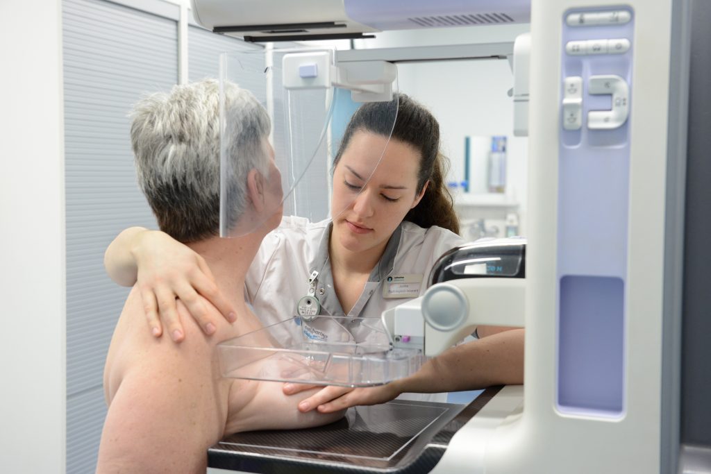 Een zorgverlener helpt een patiënt bij de mammografie en plaatst de borst op het apparaat in een kliniek.