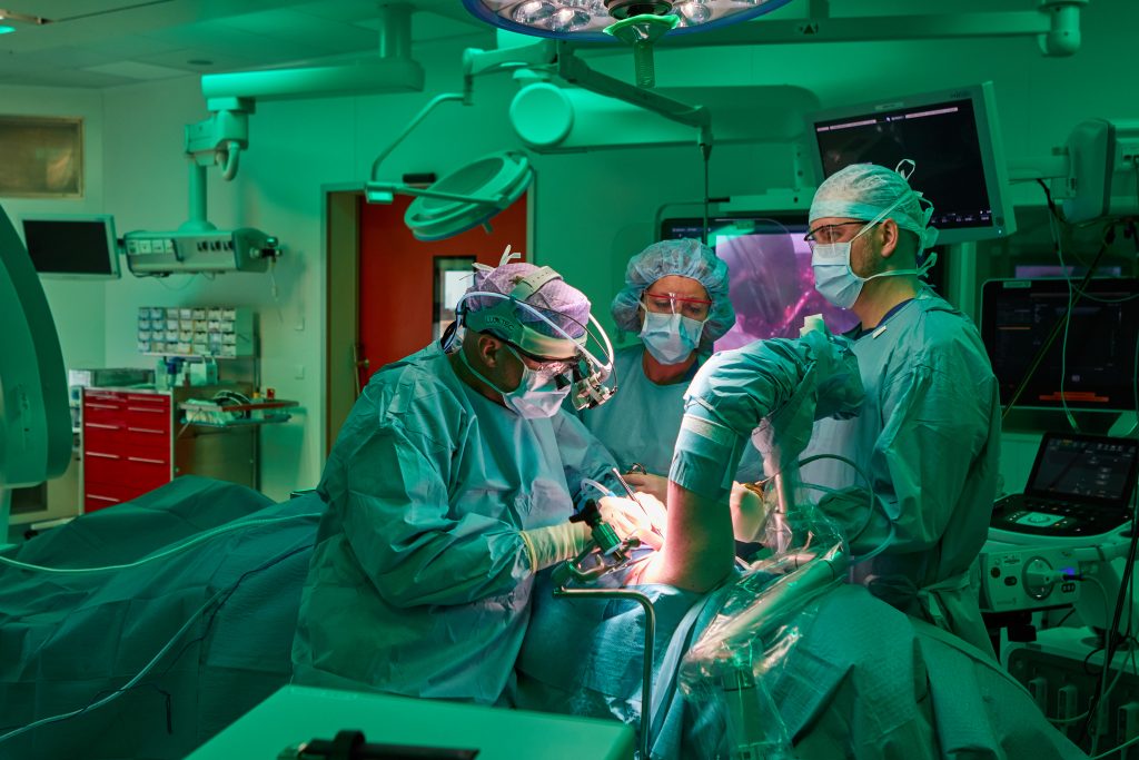 Drie chirurgen opereren een patiënt met Thoracic Outlet Syndroom in een heldere OK, omringd door medische apparatuur.