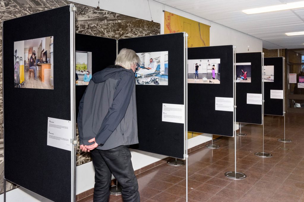 Een persoon met grijs haar bekijkt een foto op Dutch Design Week bij een tentoonstelling over de zorg van de toekomst.