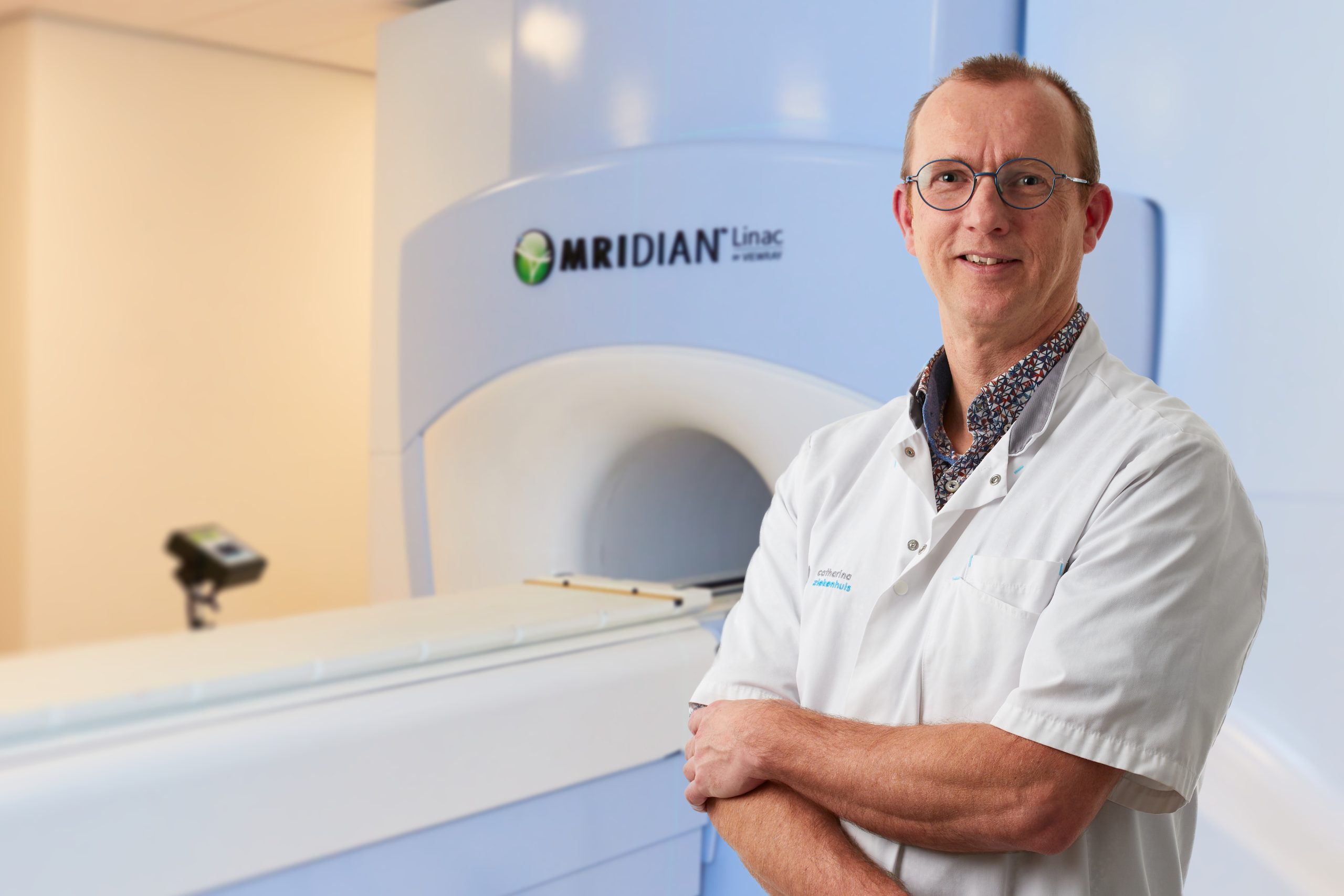 Een klinische fysicus met bril en witte jas staat met gekruiste armen voor een MRIdian Linac MRI in het Catharina Ziekenhuis.
