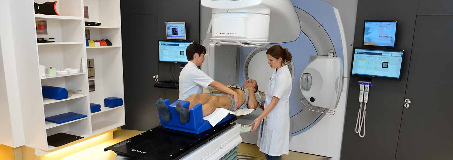 Twee artsen bereiden een patiënt voor op een behandeltafel voor radiotherapie met een groot bestralingstoestel in een kliniek.