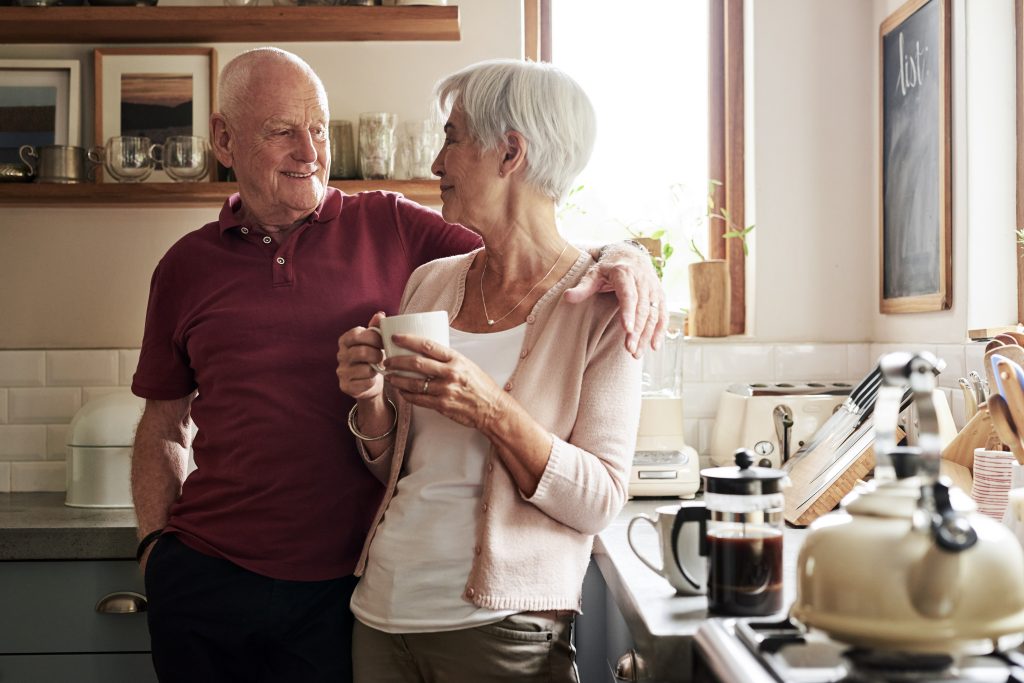 Een oudere man en vrouw staan in een zonnige keuken, drinken koffie. Een gids over hartfalen ligt op het aanrecht.