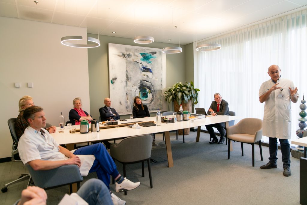 Groep mensen, deels in medische kleding, aan vergadertafel bij Catharina Ziekenhuis. Man in witte jas spreekt staand.