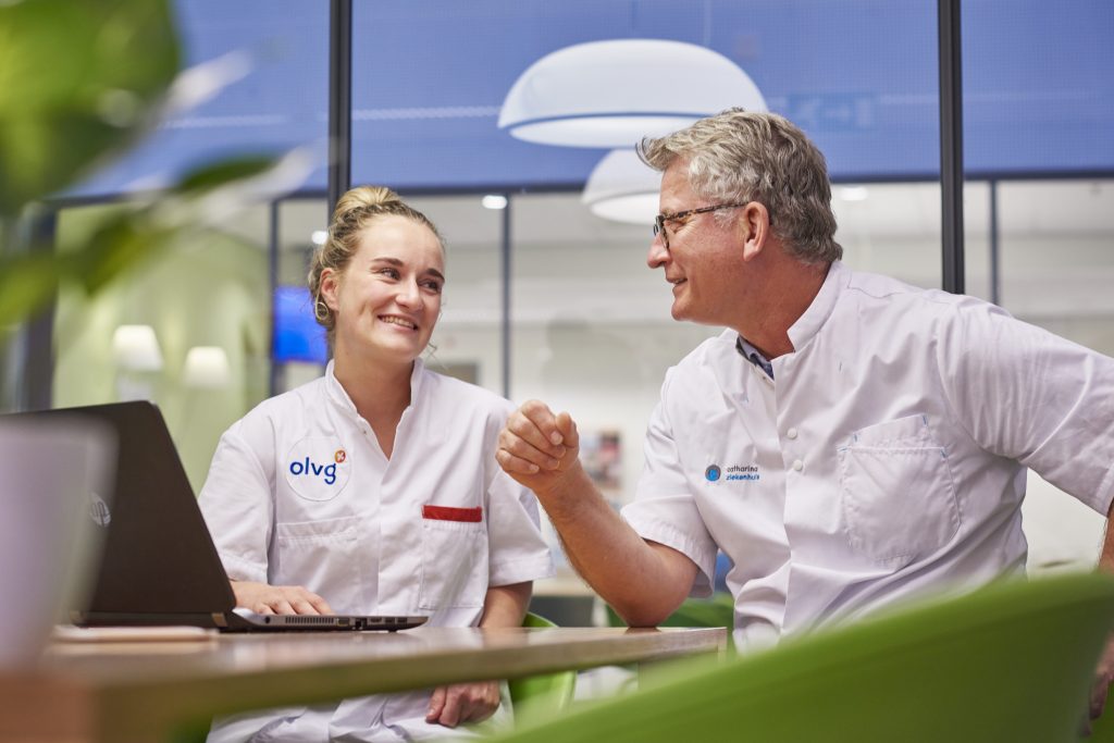 Twee medische professionals in witte uniformen werken met een laptop aan HIPS-oplossingen in een moderne, lichte kantoorruimte.