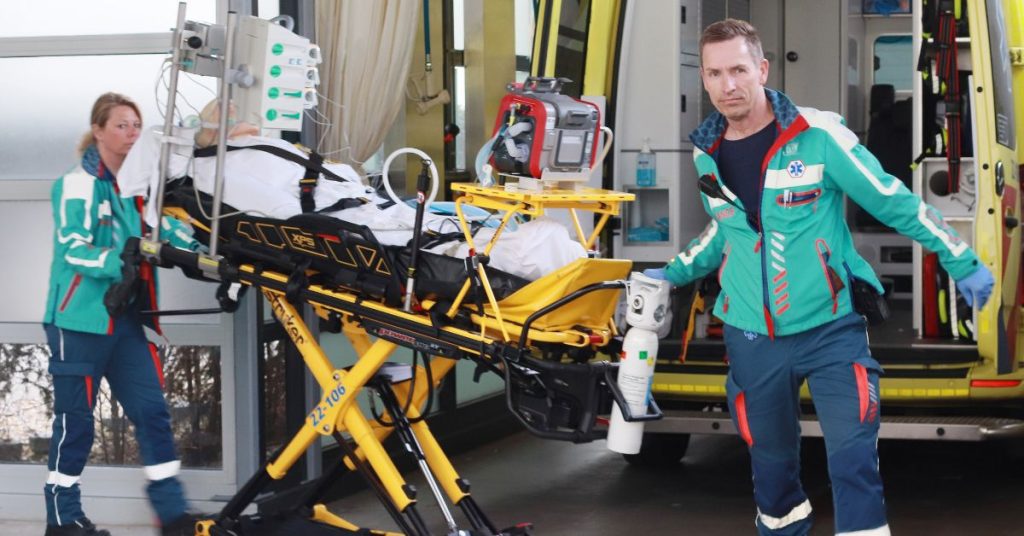 Twee ambulancemedewerkers brengen een patiënt op een brancard en medische apparatuur een gebouw binnen voor spoedtransport.