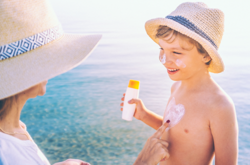 Volwassene smeert zonnebrandcrème op het gezicht en de borst van een lachend soort met strohoeden aan het strand.