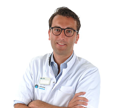 Man met bril en witte jas staat met gekruiste armen en glimlach. Plastisch chirurg gespecialiseerd in zorg voor vrouwen.