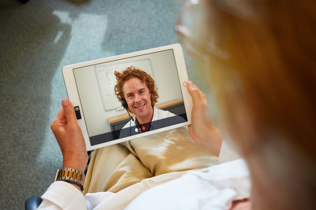 Persoon met tablet voert digitale voorlichting uit met lachende man in pak en koptelefoon; gezicht van man duidelijk op scherm.