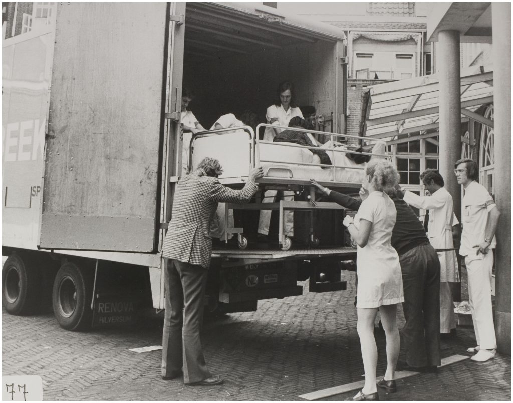 Enkele mensen laden een ziekenhuisbed met patiënt via een helling een vrachtwagen in bij het Catharina Ziekenhuis.