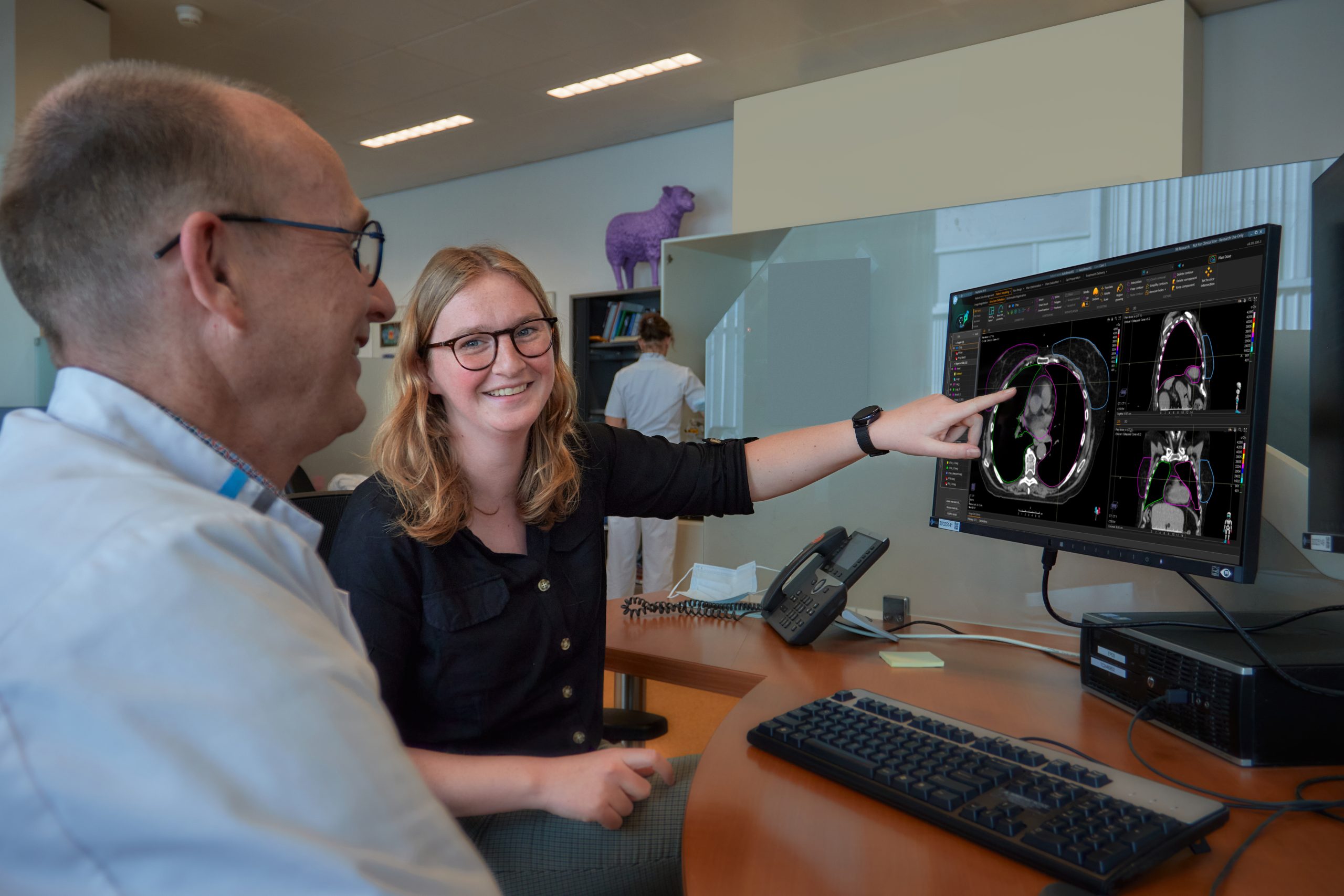 Twee personen bekijken medische scans op een computerscherm in het Catharina Ziekenhuis. Paarse dierfiguur op de achtergrond.