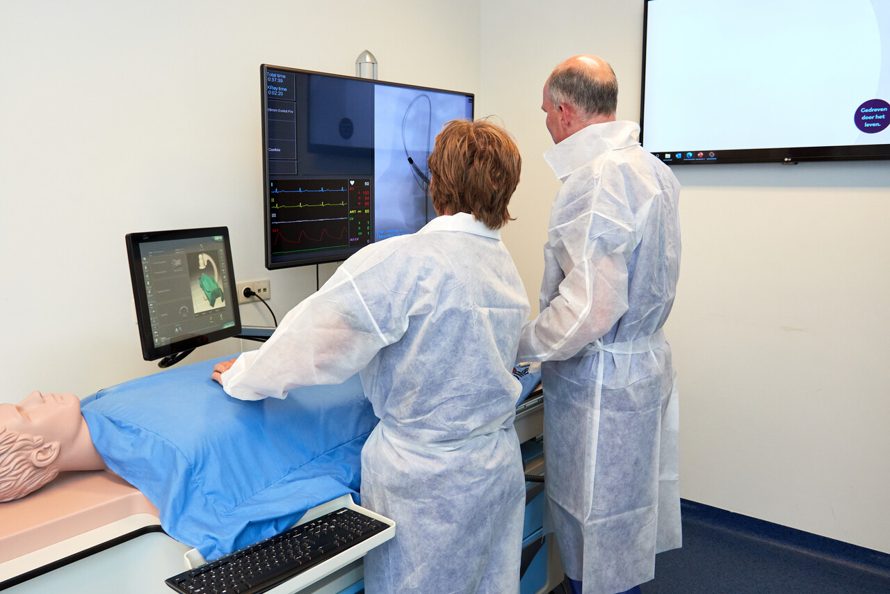 Twee personen oefenen hartoperaties op een simulator in het Catharina Ziekenhuis, met monitors, toetsenbord en muis in beeld.