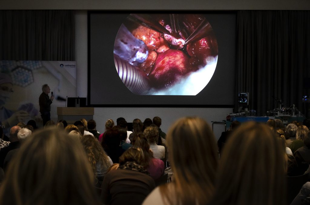 Tijdens Hartweek in het Catharina Ziekenhuis bekijken zorgprofessionals in een zaal een operatie op groot scherm met uitleg van een spreker.
