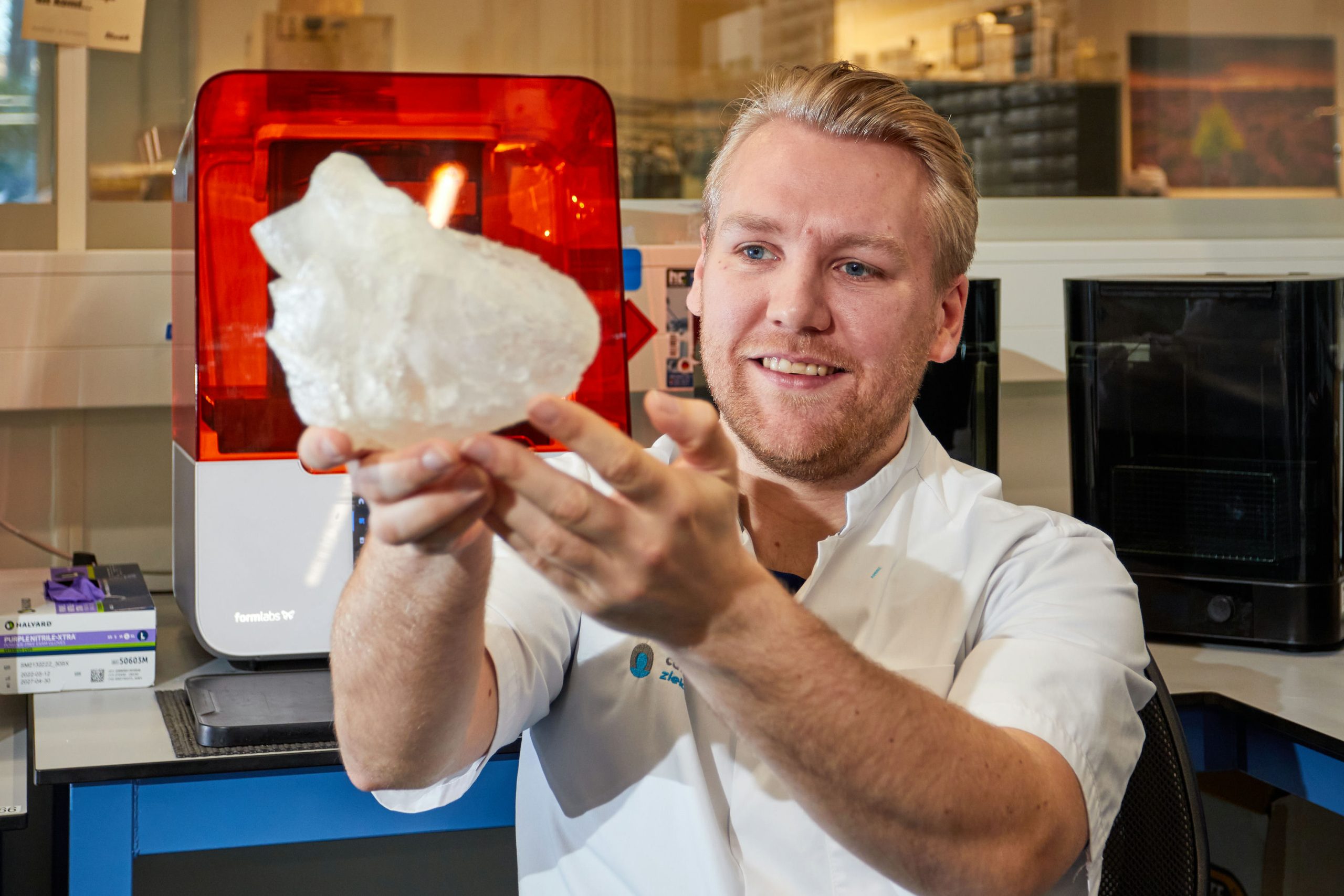 Man in witte labjas toont groot transparant 3D-geprint object in laboratorium voor innovatie mitralisklepchirurgie.