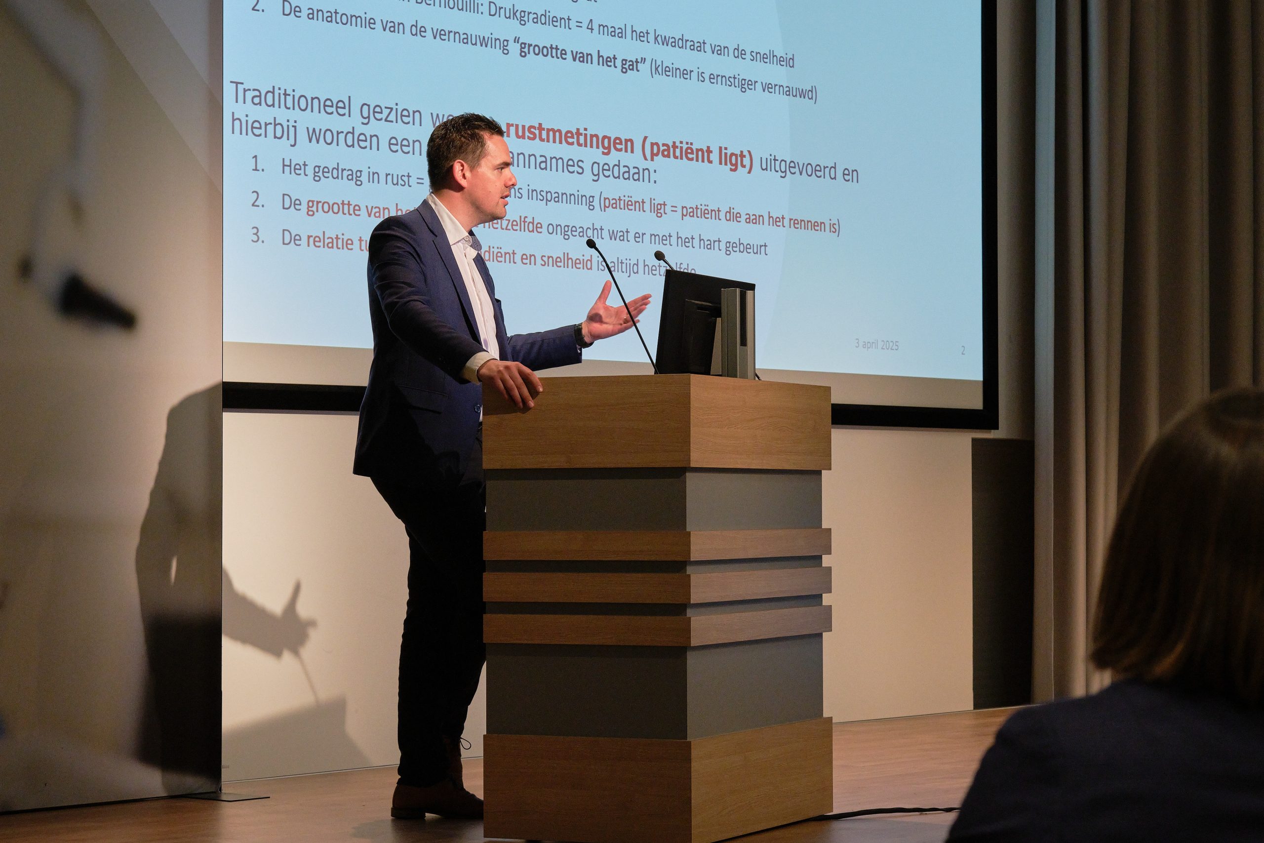 Op Wetenschapsavond 2025 geeft een man in pak een presentatie bij een katheder, met Nederlandse tekst achter hem.