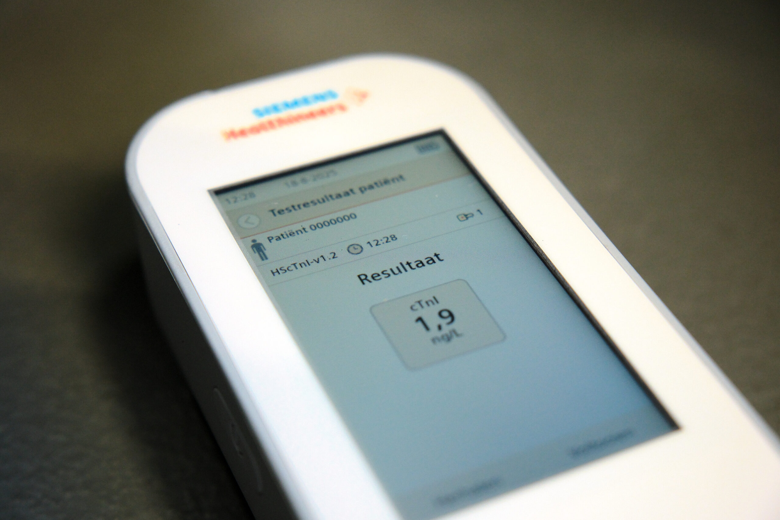 Wit handapparaat voor sneltest hartinfarct toont "Resultaat" en cTnl 1.9 ng/L op scherm; donkere, gladde ondergrond.